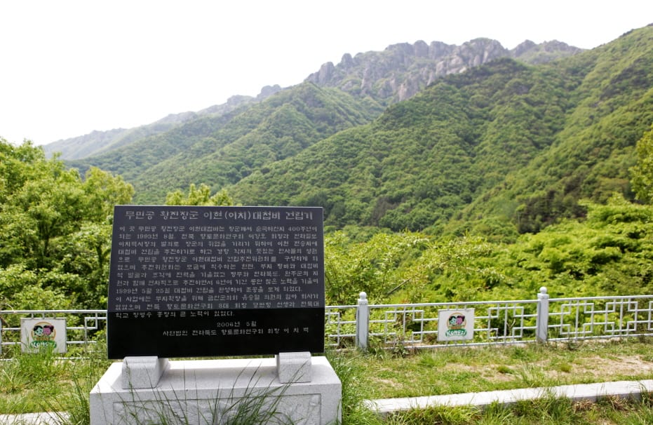 황진 장군 이치대첩비 건립기를 새긴 검은 비석, 뒤로 숲 너머 대둔산 바위 능선