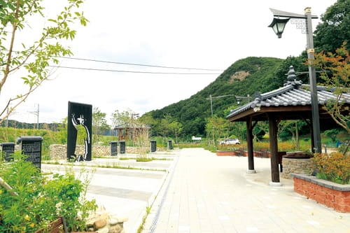 검은 오석 안내판과 손을 든 정여립 조형물, 정자가 놓인 공원 산책로