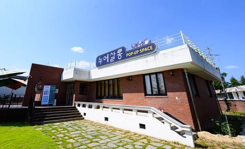'누에살롱' 간판을 단 붉은 벽돌 건물과 잔디 마당