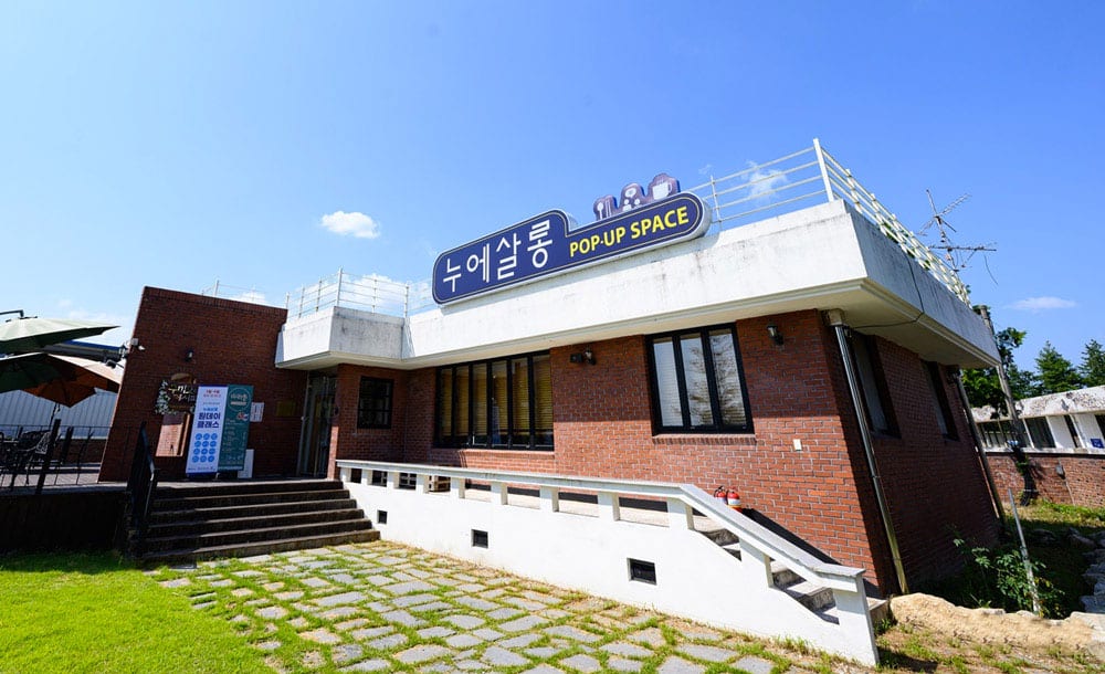 '누에살롱' 간판을 단 붉은 벽돌 건물과 잔디 마당