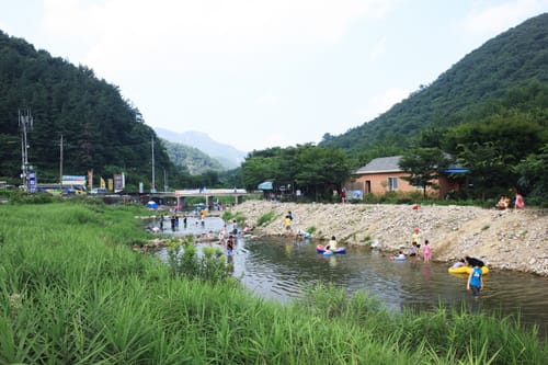 산골 마을 다리 아래 넓은 냇물에서 물놀이하는 사람들