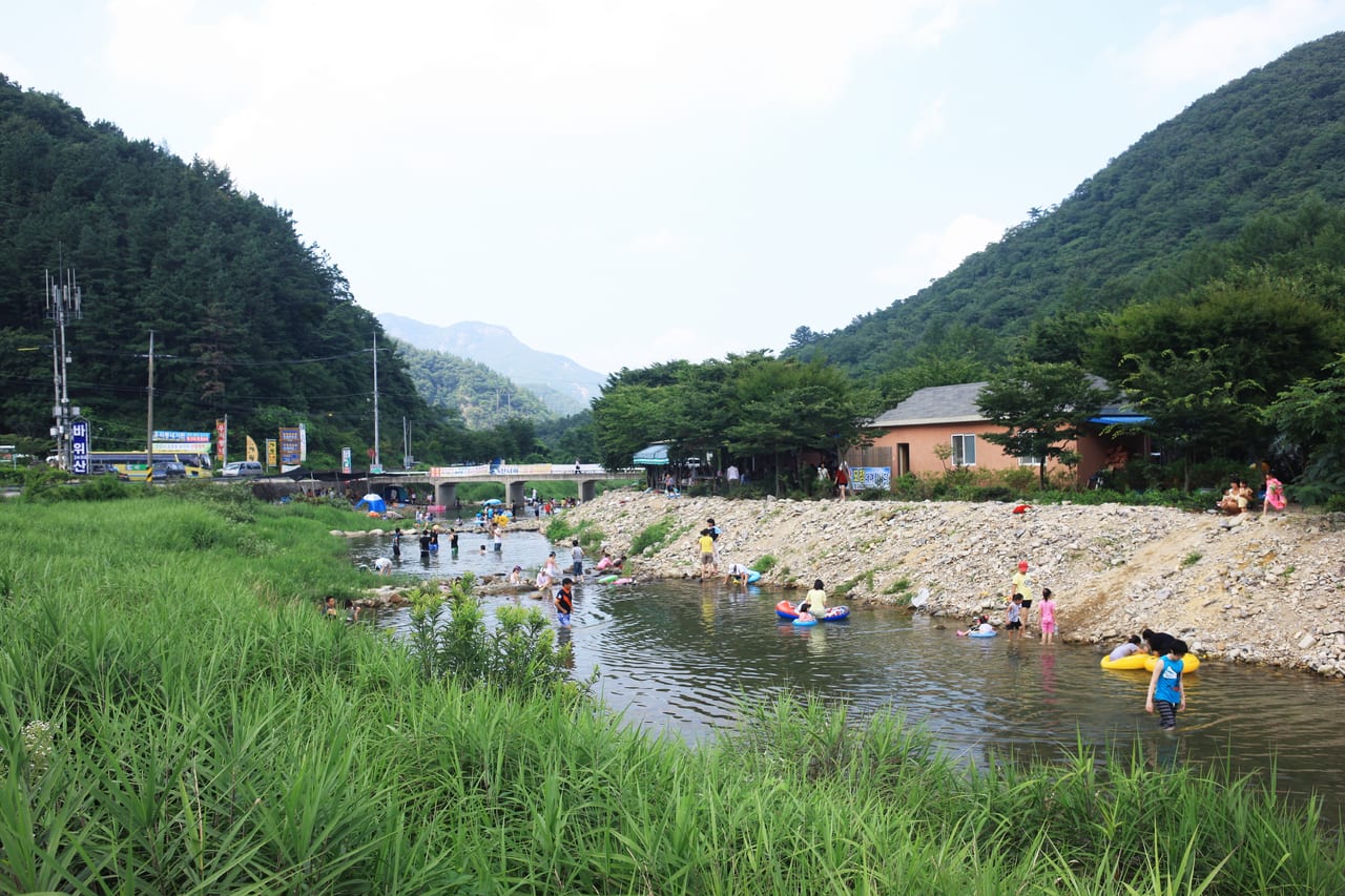 산골 마을 다리 아래 넓은 냇물에서 물놀이하는 사람들