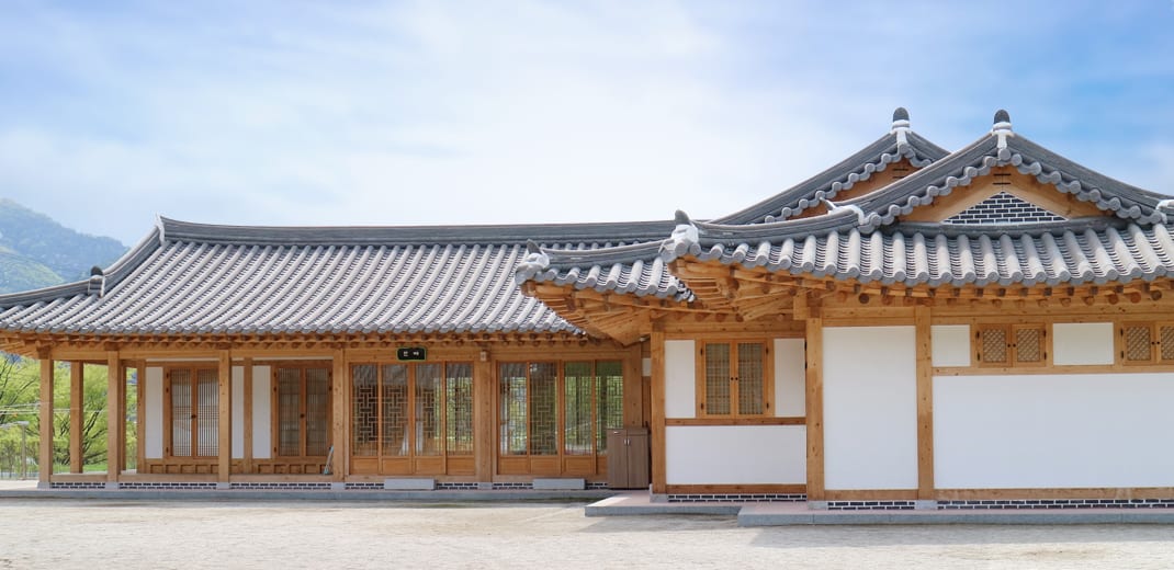 넓은 마당 앞에 선 새 한옥 건물, 나무 기둥과 창호가 이어진 기와집